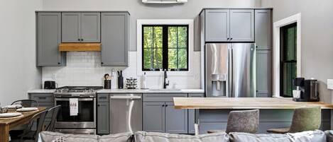 Una cocina moderna con gabinetes grises, un refrigerador de acero inoxidable y una ventana con vista a árboles.