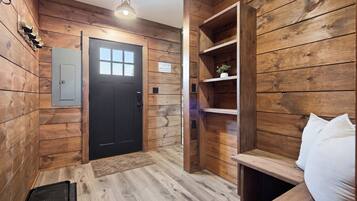 Un intérieur en bois avec une porte noire, une étagère ornée d’une plante et un coussin blanc.