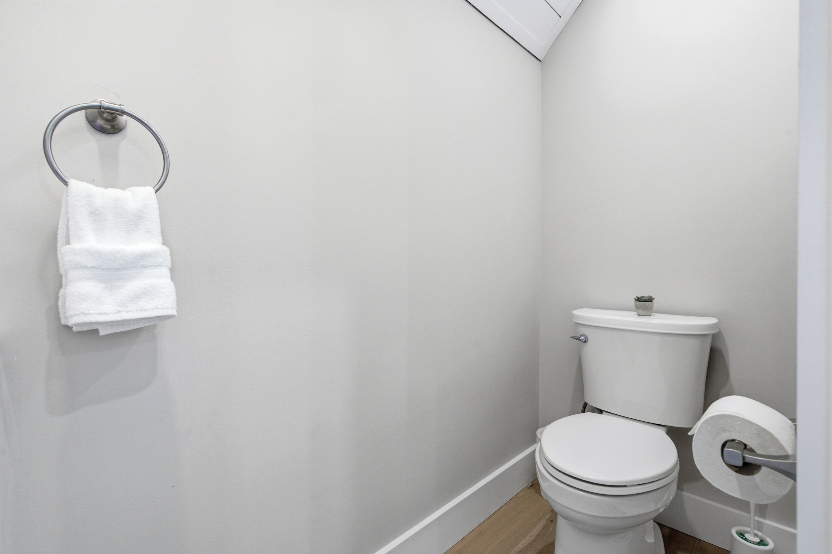 Een kleine, schone badkamer met toilet, een handdoekhouder met een opgevouwen handdoek en een toiletrolhouder.