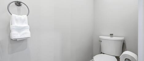 Een kleine, schone badkamer met toilet, een handdoekhouder met een opgevouwen handdoek en een toiletrolhouder.