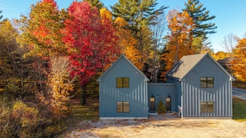 Una casa di legno blu a due piani, con un design simmetrico, un camino centrale e un piccolo portico.