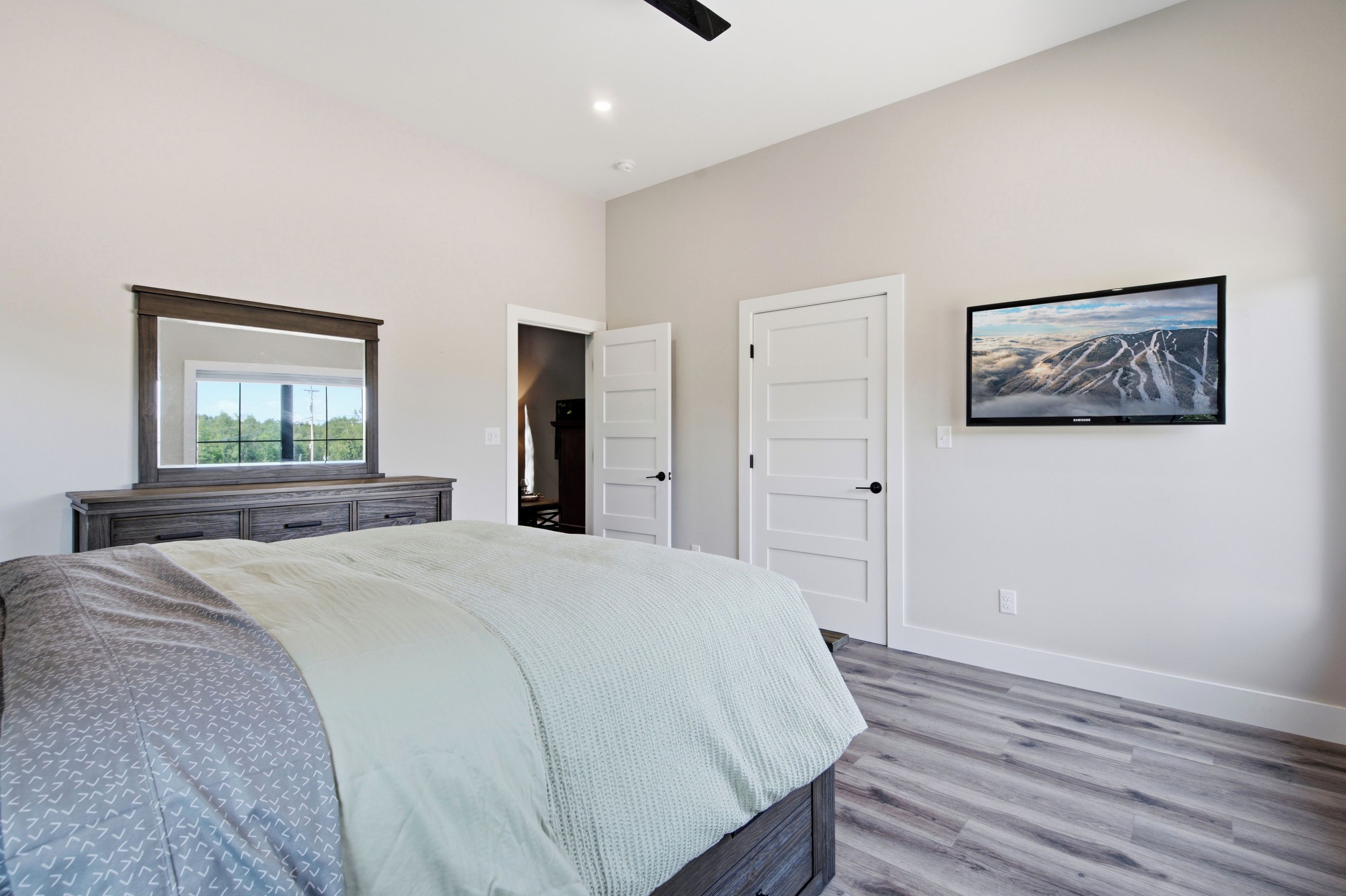 A bedroom with a bed, dresser, and a television on the wall.