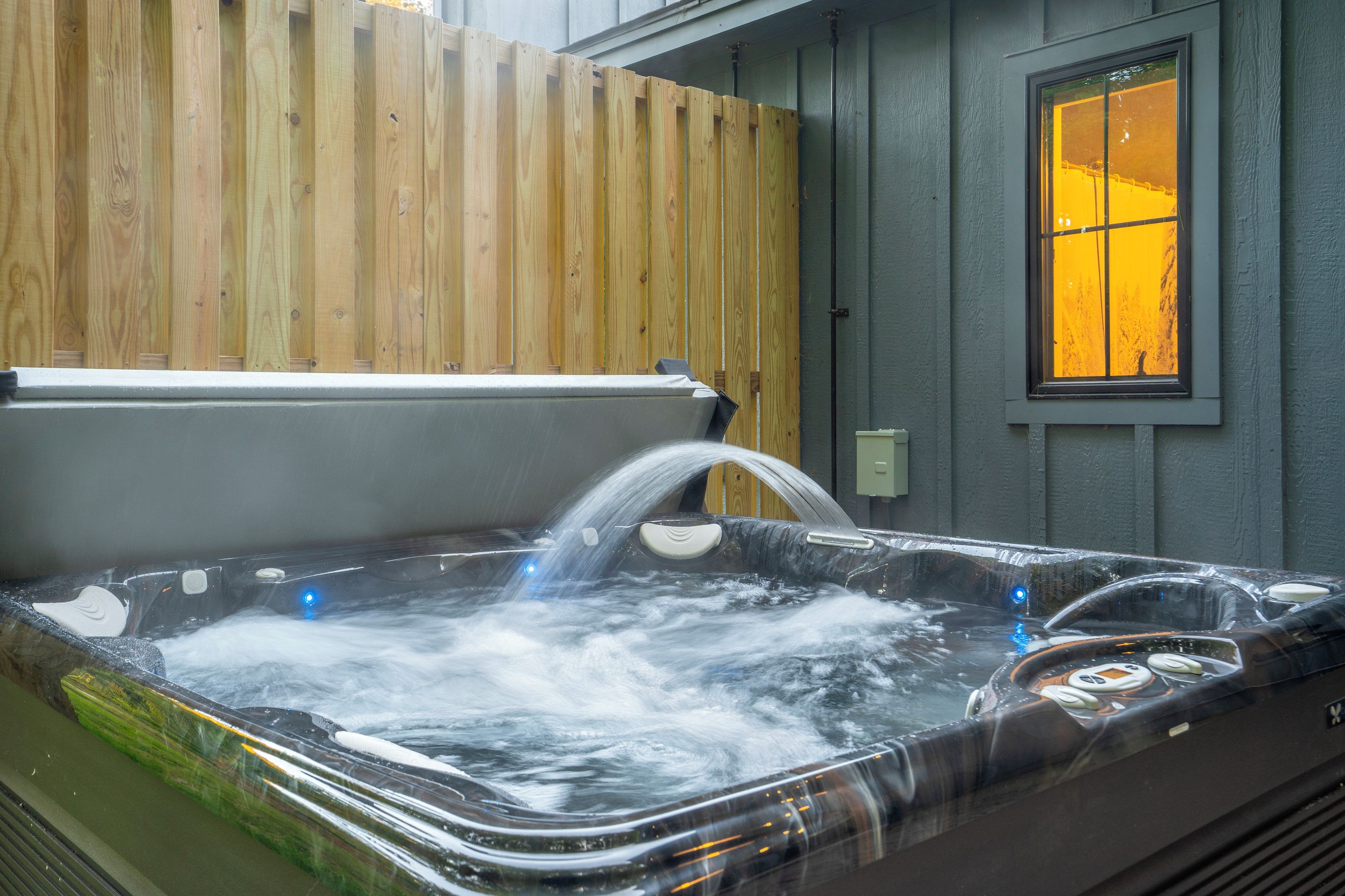 A hot tub with a wooden fence and a window with yellow light.
