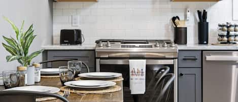 A modern kitchen with grey cabinets, a stainless steel stove, and a dining table set with plates and glasses.