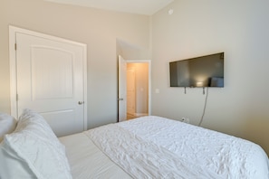 Ein Schlafzimmer mit einem großen Bett, einem an der Wand montierten Fernseher und einer Tür zu einem weiteren Raum.