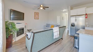 A modern living room with a fireplace, a sofa, a TV, and a kitchen area with a refrigerator and a trash bin. - Great for Groups! 2 Centrally Located Concord Gems (Concord)