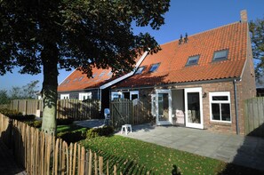 Ett tvåvåningshus med ett rött tegeltak, ett trästaket och en stenlagd uteplats.