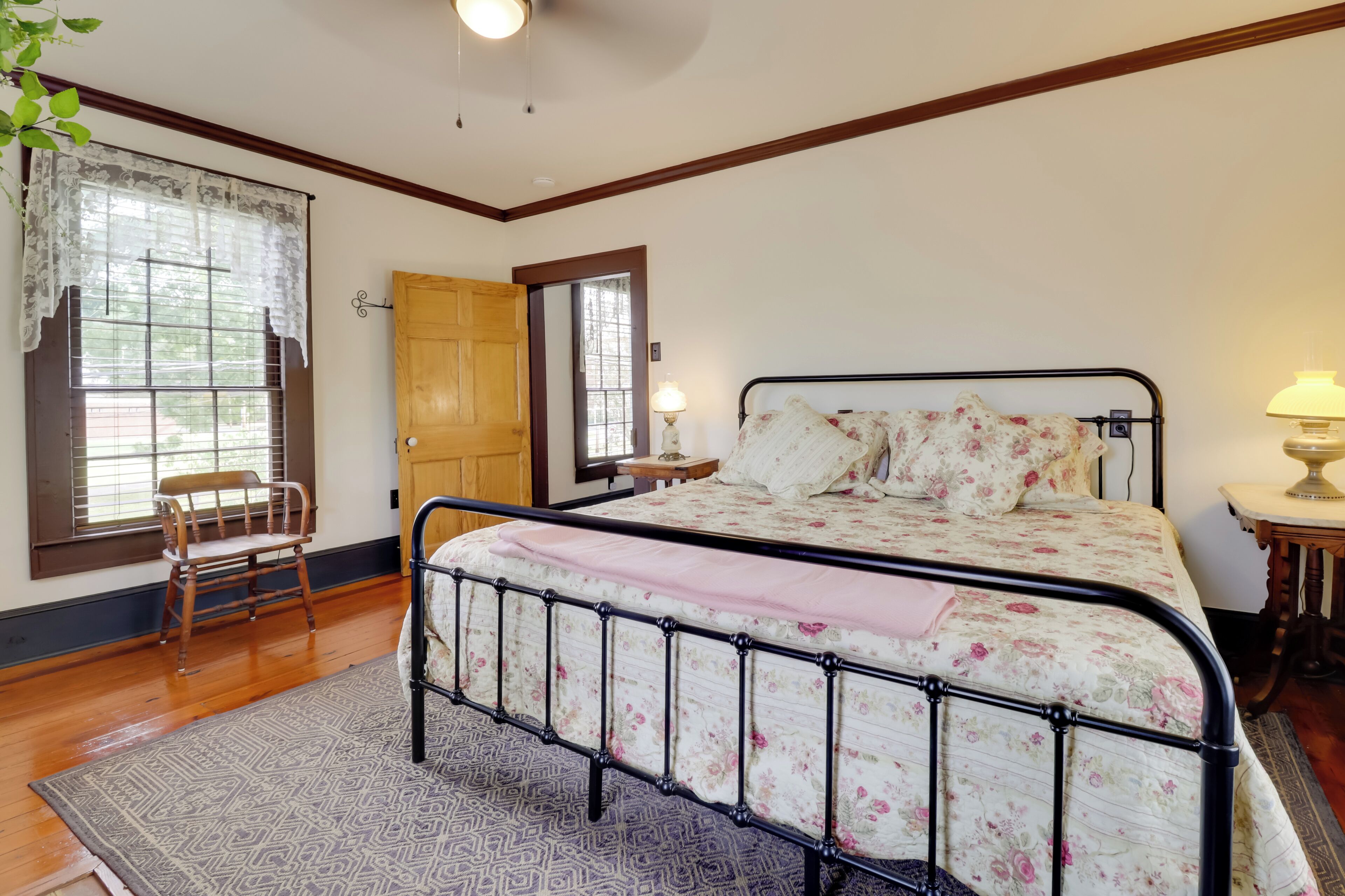 A bedroom with a bed, a chair, a wooden door, and a window with a lace curtain.