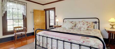 A bedroom with a bed, a chair, a wooden door, and a window with a lace curtain.