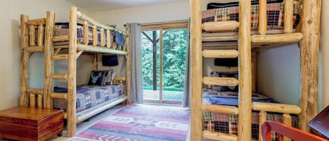 A room with a bunk bed, a desk, and a window with a view of trees.