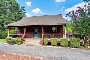 Eine Holzhütte mit Veranda, Stufen zum Eingang und einem kleinen Gartenbereich mit Topfpflanzen.