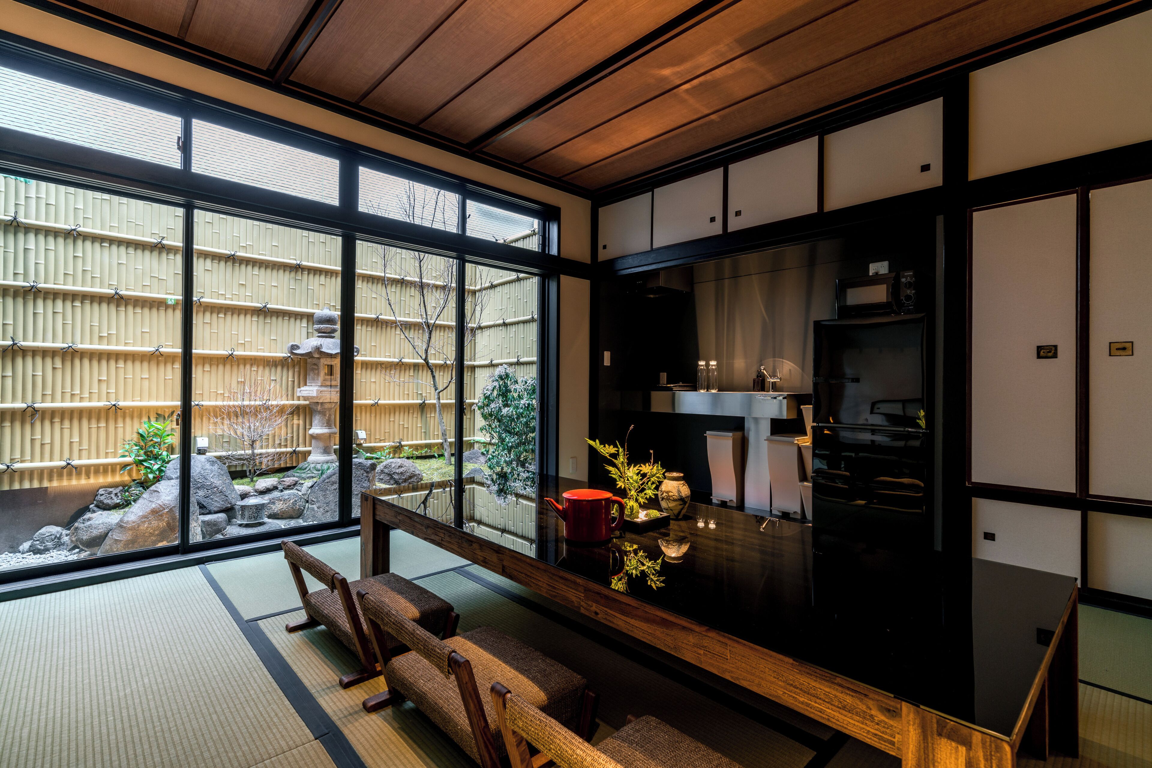 A traditional Japanese room with tatami flooring, a low table, and a view of a bamboo fence outside.