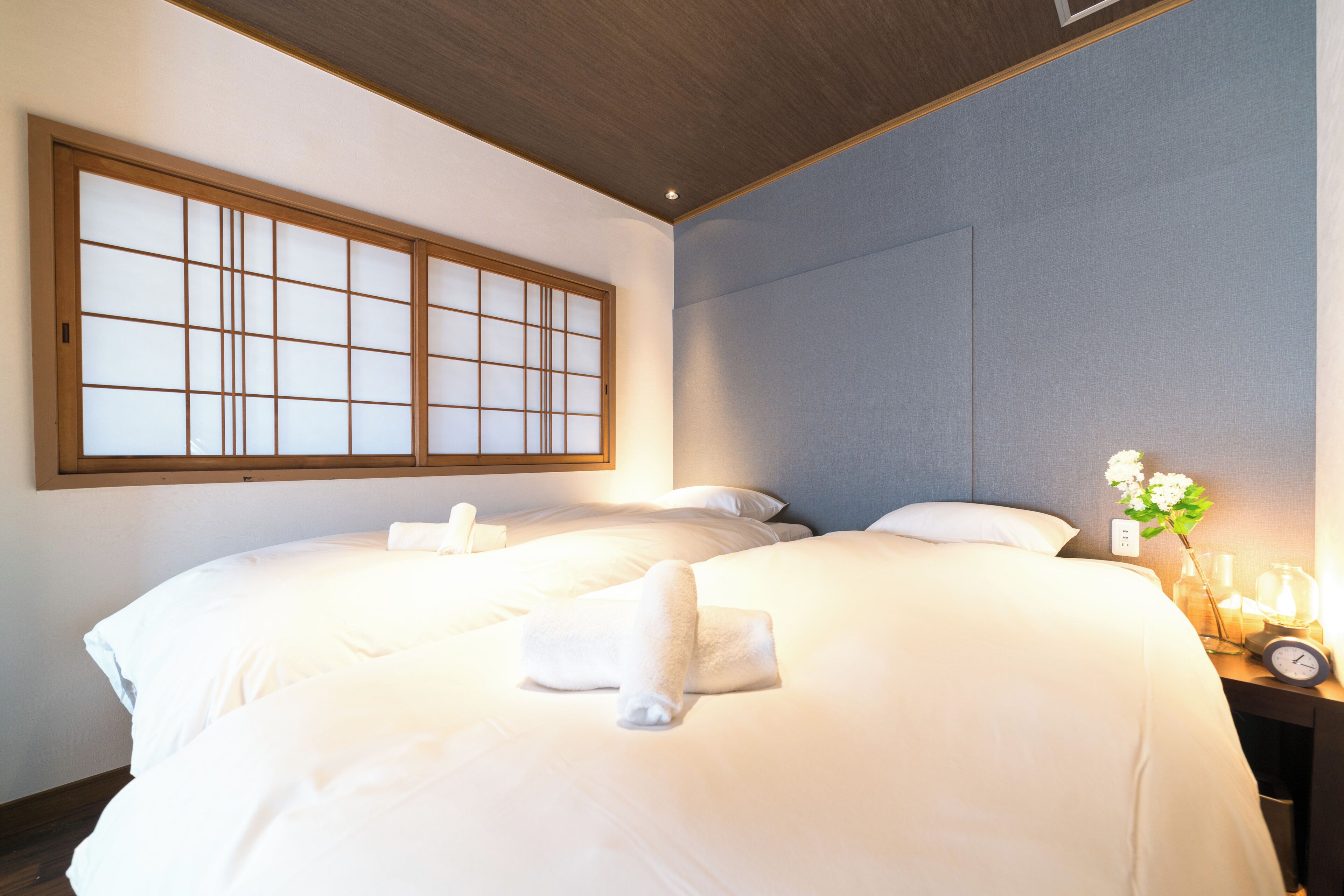 Una habitación de hotel con dos camas, un ventanal grande y una mesita de noche con una lámpara y un reloj.