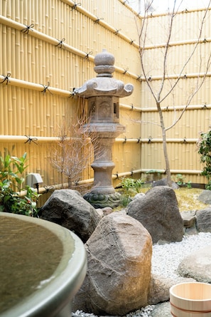 Ein traditioneller japanischer Garten mit Steintorii, Bambuszaun und großen Felsen.