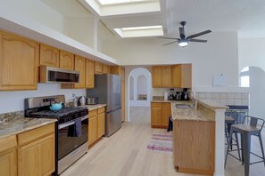 A modern kitchen with wooden cabinets, stainless steel appliances, a gas stove, and a ceiling fan.