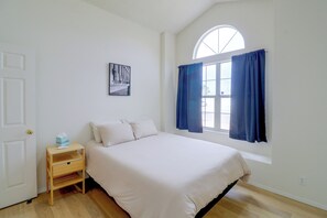 A bedroom with a bed, a nightstand, a window with curtains, and a wall-mounted picture.