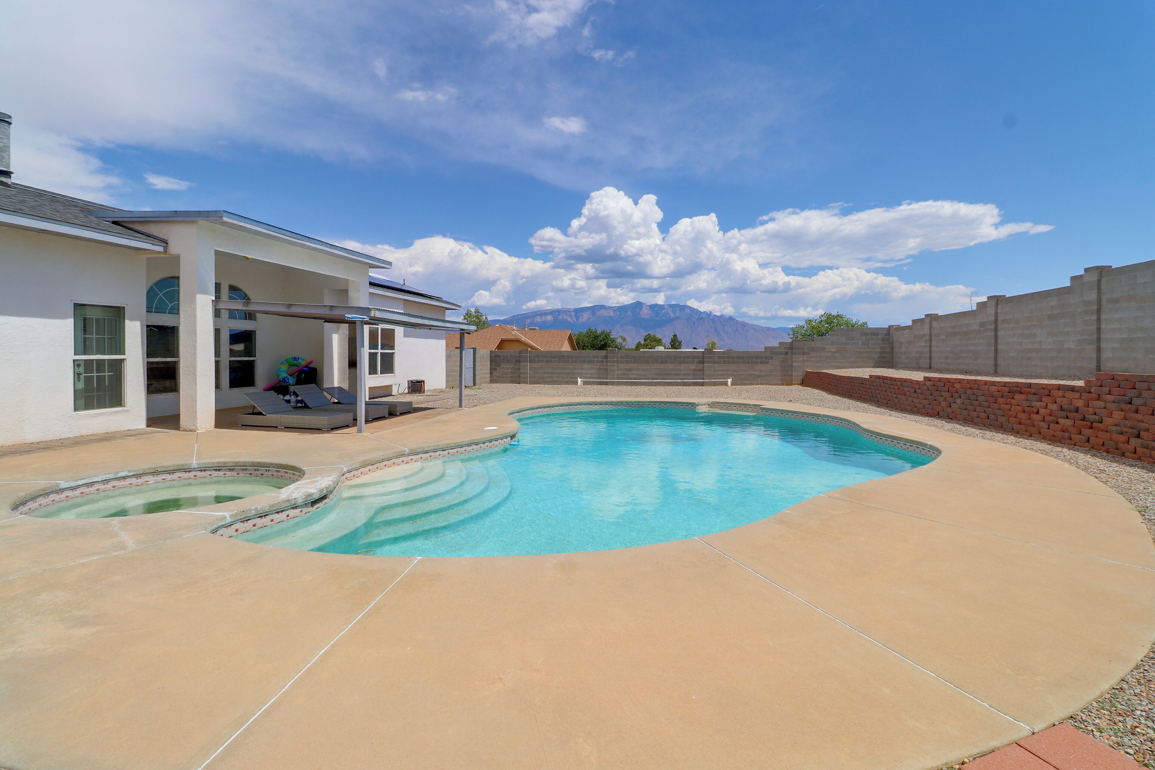 A swimming pool with a sunken hot tub, a covered patio area, and a mountain view in the background.