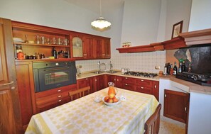 Eine Küche mit Holzschränken, einem Herd, einem Backofen und einem Esstisch mit Obstschale.