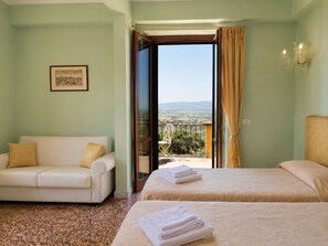 Ein Hotelzimmer mit Balkon, einer Sitzecke, zwei Betten und einem gerahmten Bild an der Wand.