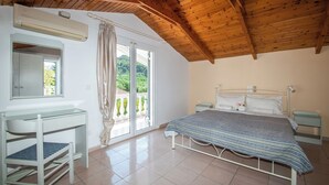 Un dormitorio con techo de madera, una cama con cubrecama estampado, una mesita de noche y un espejo, además de un ventanal con cortinas.