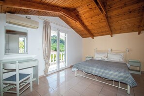 Un dormitorio con techo de madera, una cama con cubrecama estampado, una mesita de noche y un espejo, además de un ventanal con cortinas.