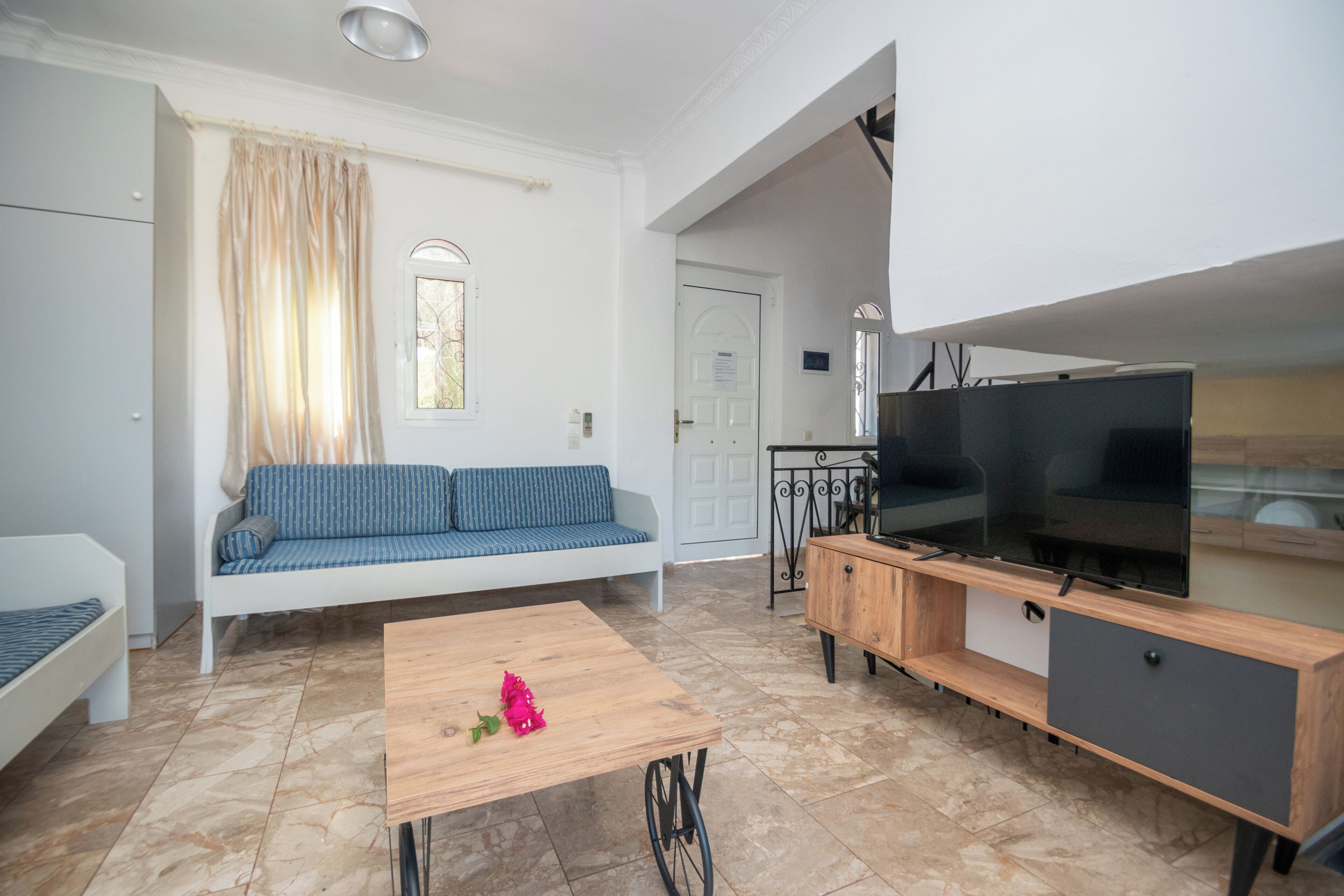 A modern living room with a sofa, a coffee table with flowers, a TV, and a dining area.