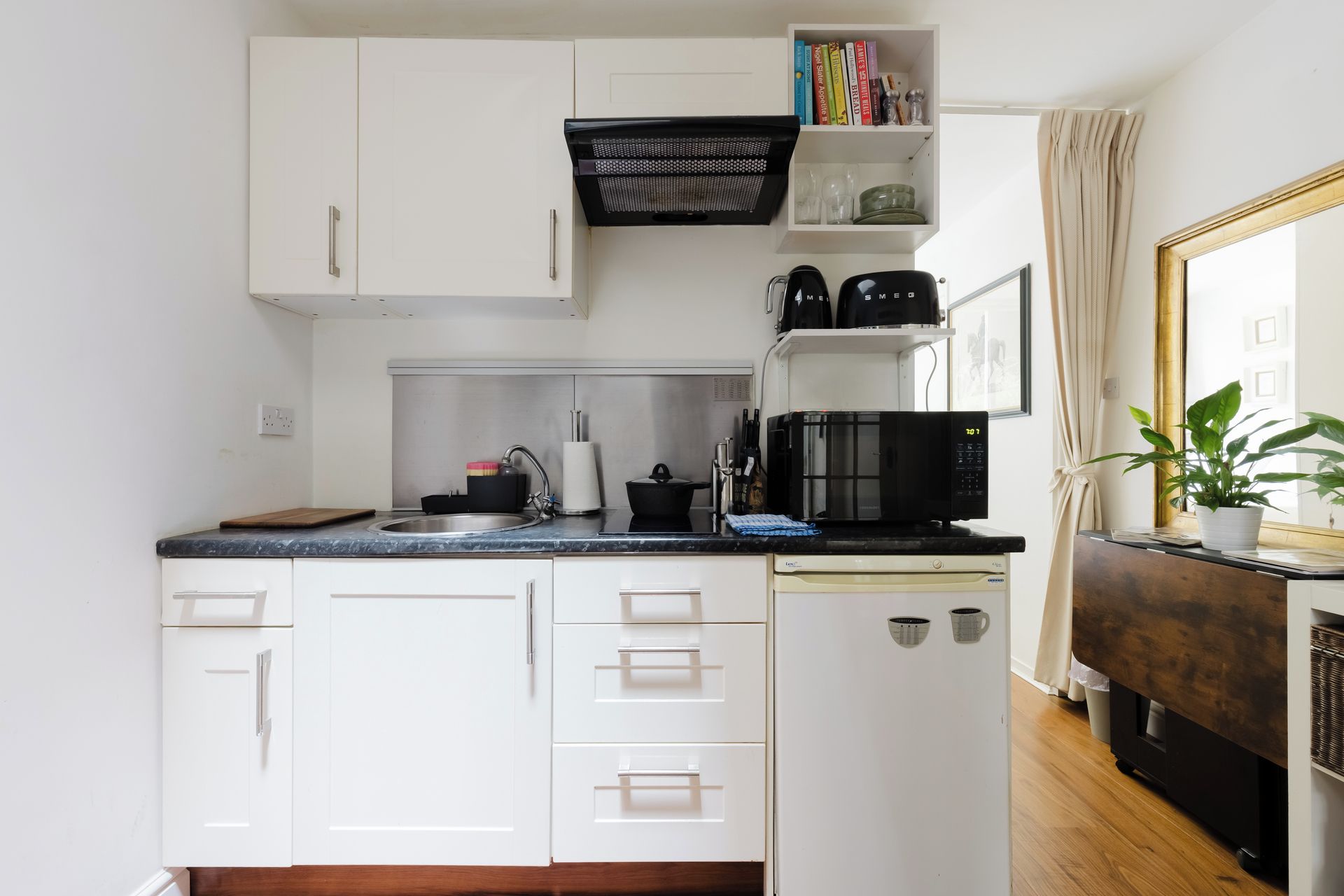 Een kleine keuken met witte kasten, een zwarte magnetron en een spoelbak.