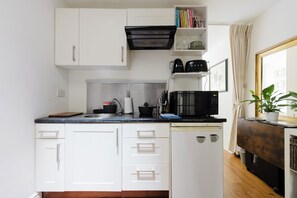A compact kitchen with white cabinets, a black microwave, and a sink. - Refined 1BDR Retreat in the Heart of Clapham (Greater London)