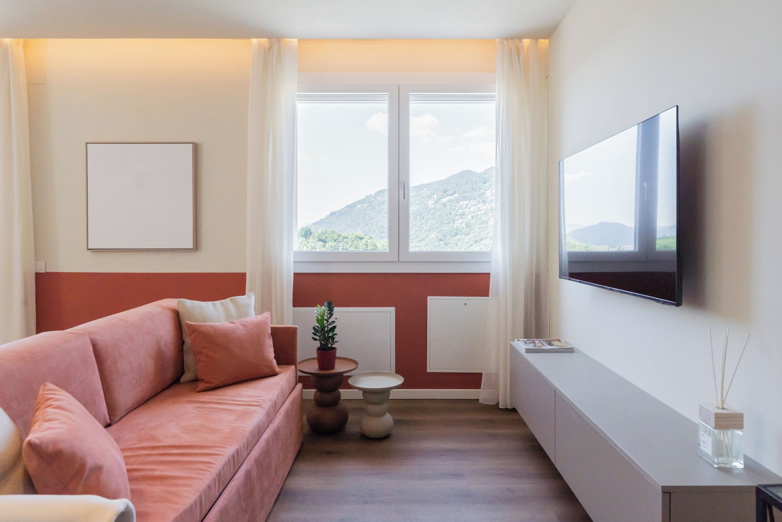 Una sala moderna con un sofá, una mesita, una planta en maceta y un televisor de pantalla plana montado en la pared.