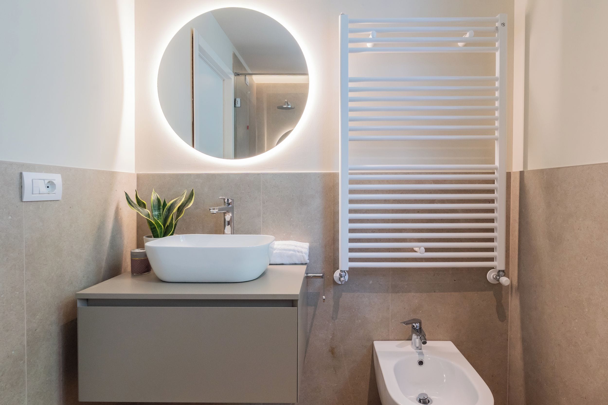 Ein modernes Badezimmer mit rundem Spiegel, einem Aufsatzwaschbecken, einem Bidet und einem Handtuchhalter.
