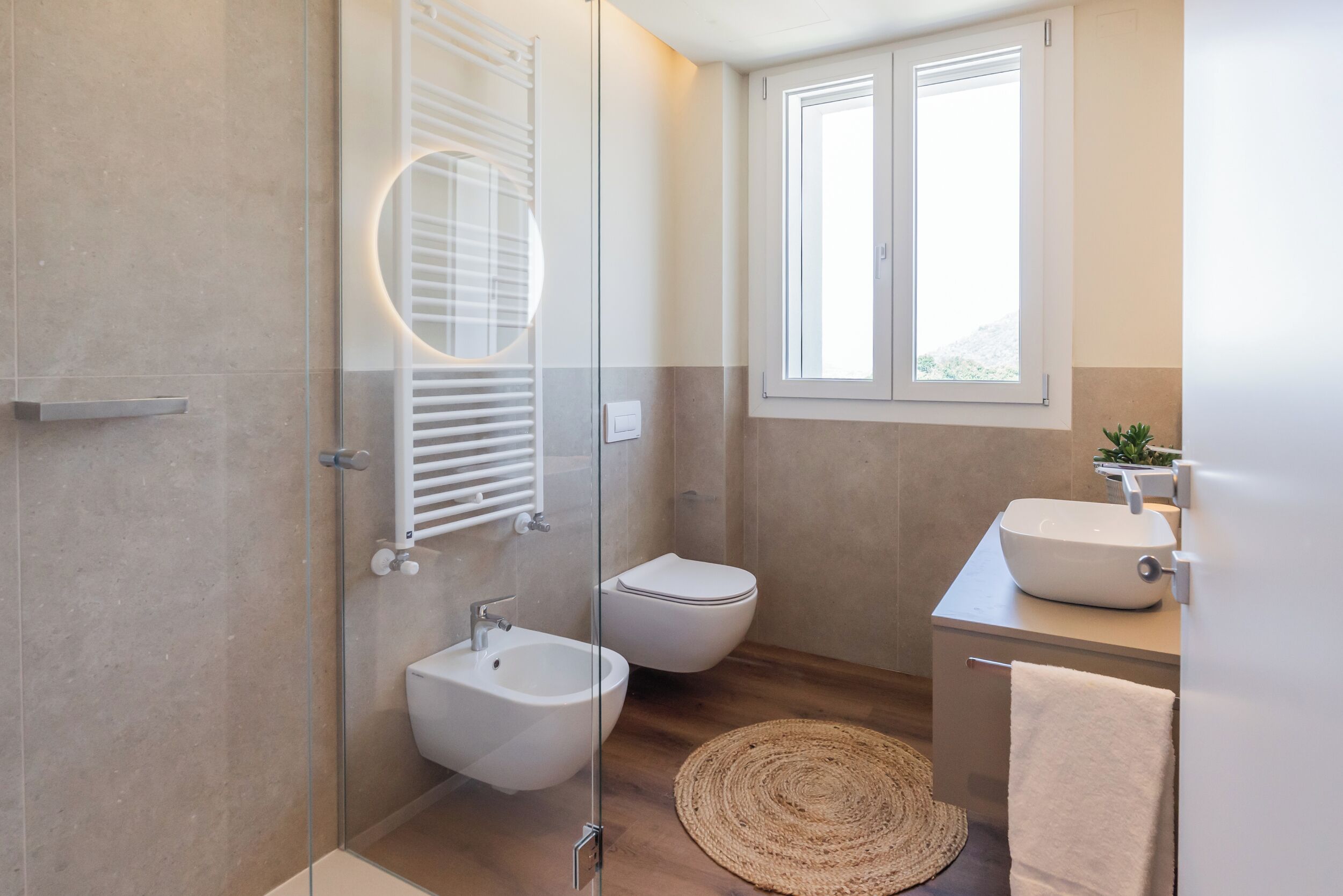 A modern bathroom with a glass shower enclosure, a bidet, a toilet, and a sink with a mirror.