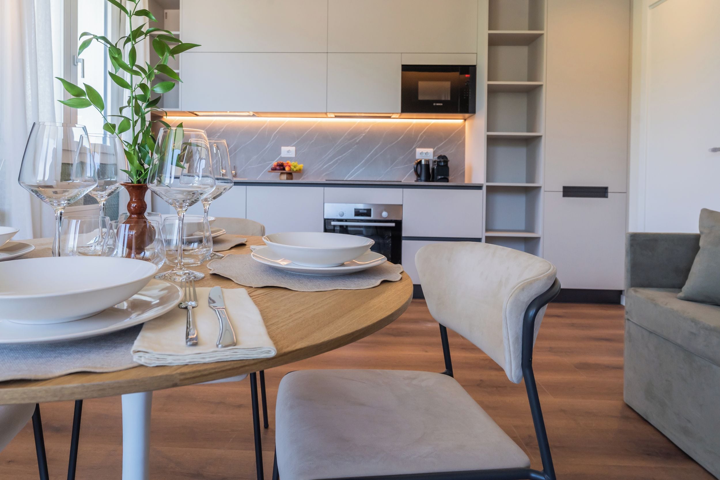 Una cucina moderna con forno integrato e zona pranzo con tavolo rotondo apparecchiata per un pasto.