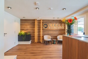 A reception area with a wooden wall, a sign reading 'Circle Bike Residence,' two chairs, a plant, and a vase with flowers. - Circle Bike Residence by Rent All Como. (Tavernerio)