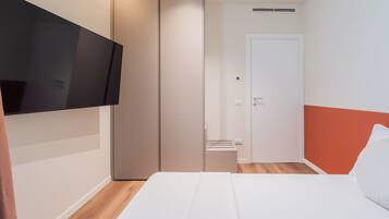 A bedroom with a bed, a wardrobe, a television mounted on the wall, and a door.