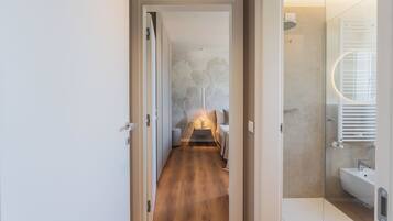 A hallway leading to a bedroom with a bed, bedside table, and a wall with a floral pattern.
