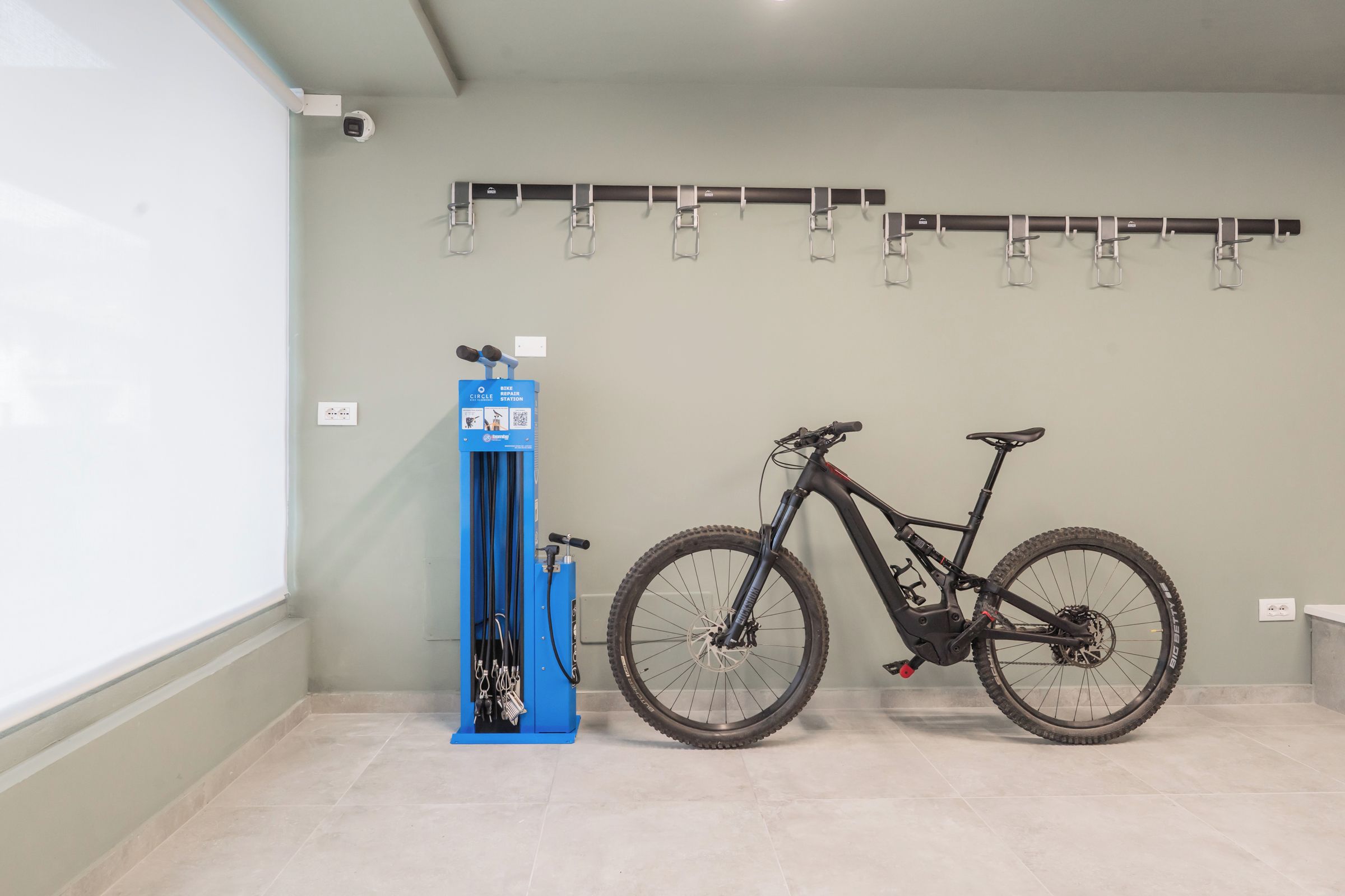 Una estación de reparación de bicicletas con una bicicleta y una bomba para neumáticos en una habitación con suelo de baldosas y un soporte de bicicletas en la pared.