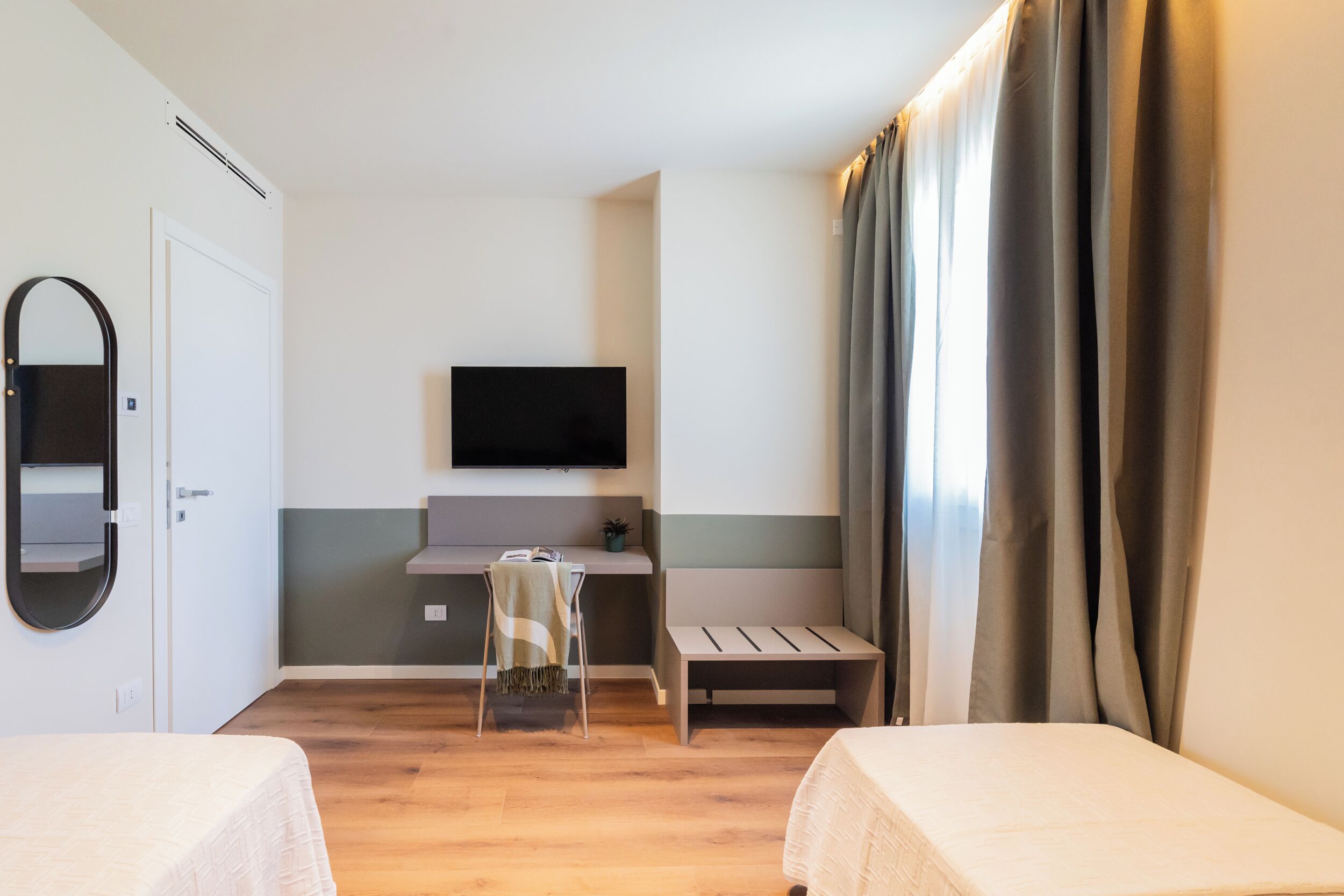 Ein Hotelzimmer mit einem Bett, einem Schreibtisch, einem Sessel, einem Fernseher und einem Fenster mit Vorhängen.