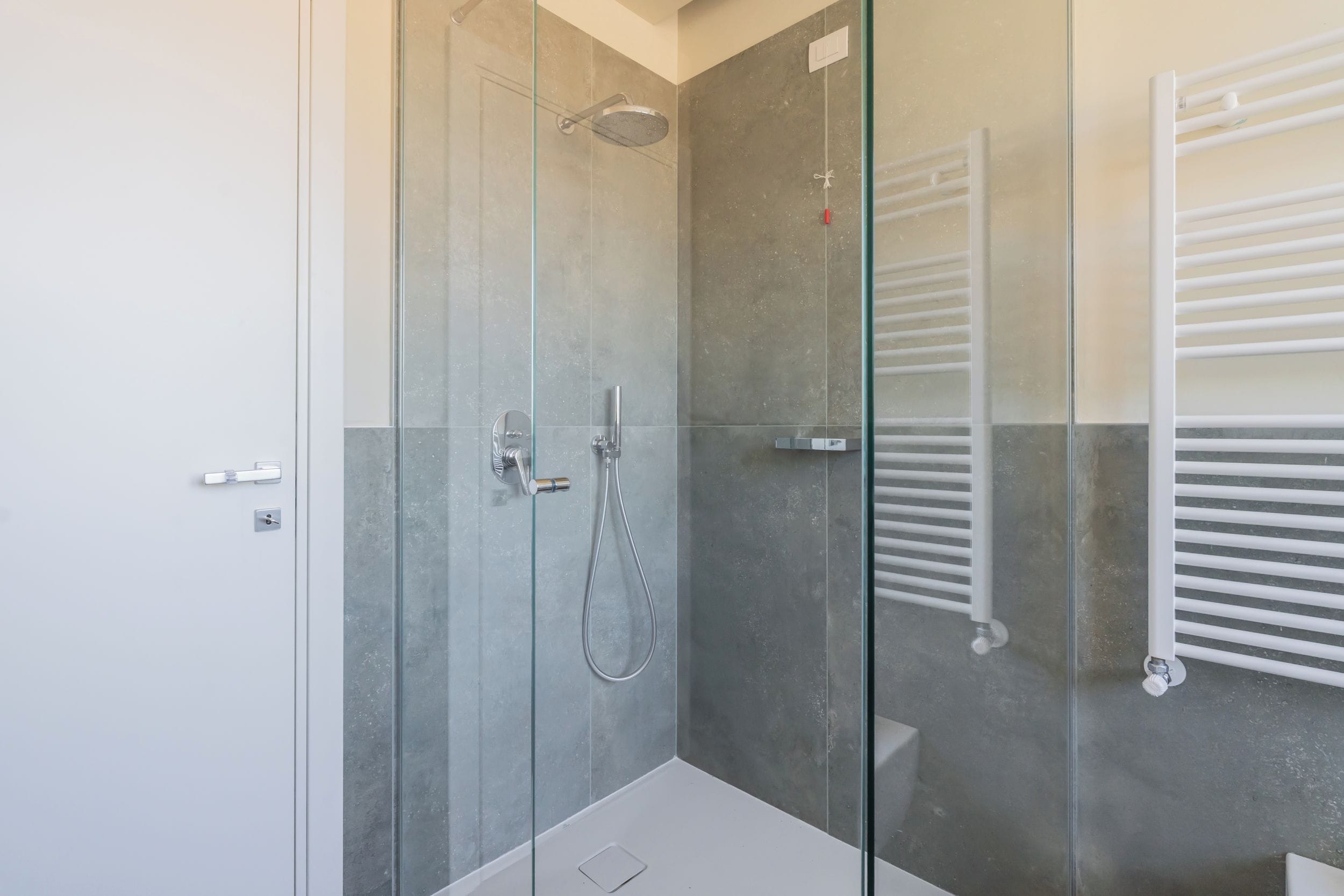 A modern bathroom with a glass-enclosed shower, a white bathtub, and a white towel rack.