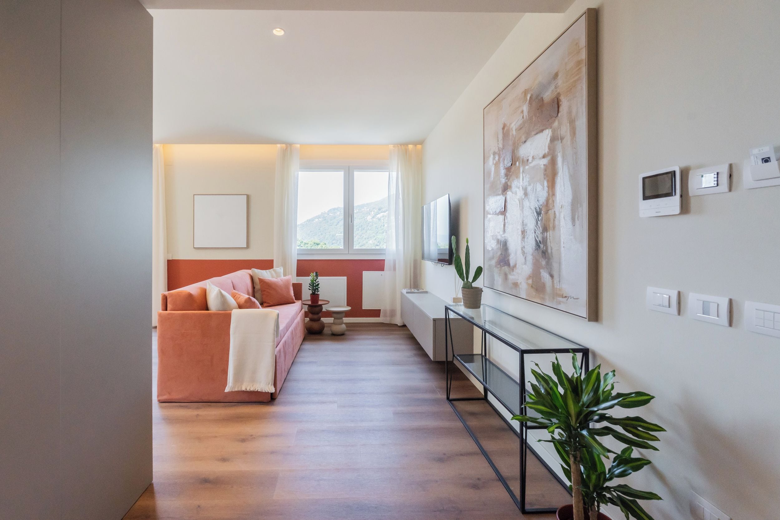 A modern living room with a sofa, a flat-screen TV, a large abstract painting, and a potted plant.