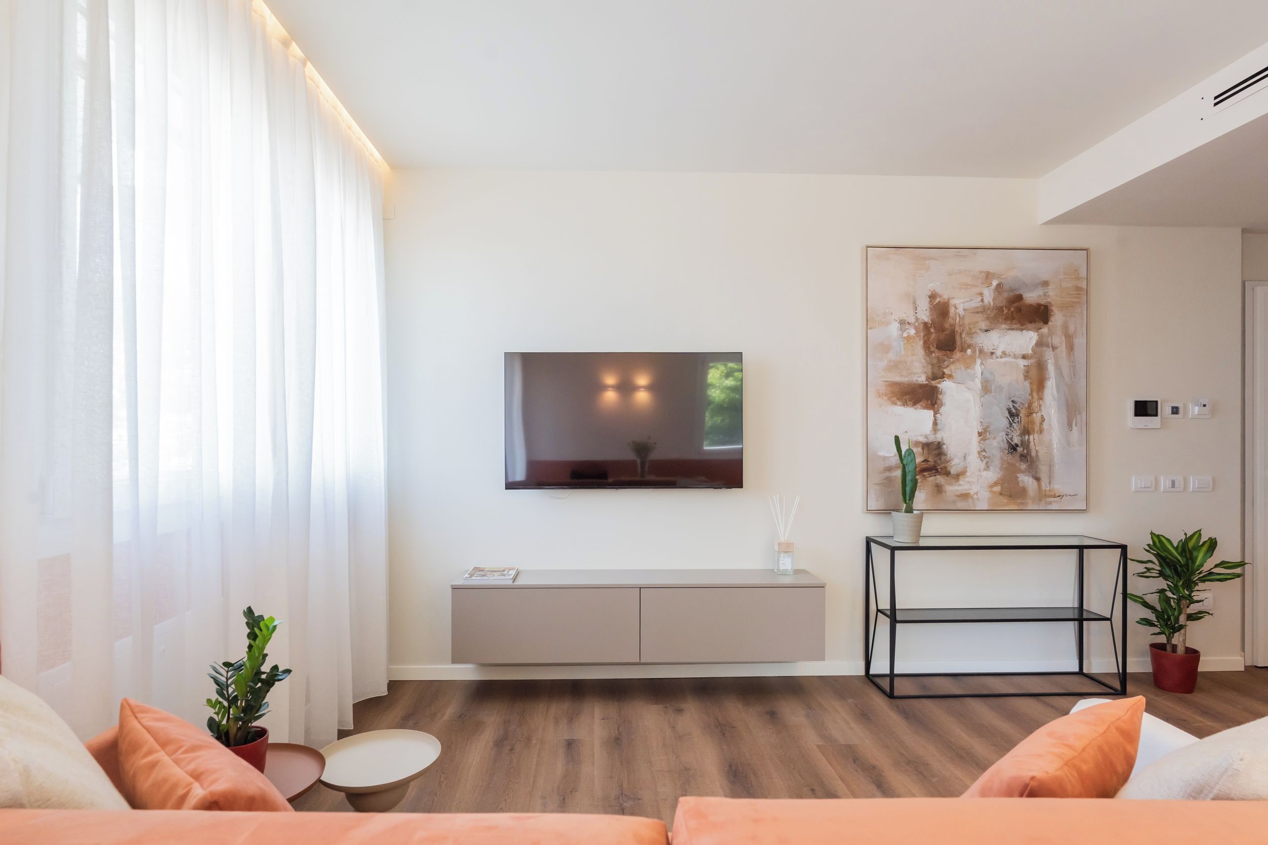A modern living room with a flat-screen TV mounted on the wall, a minimalist console table, and a large abstract painting.