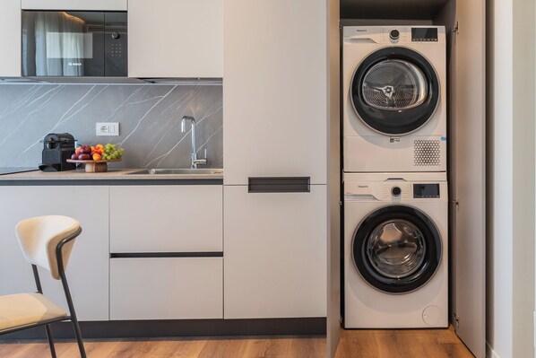 A compact kitchen with a built-in washing machine, a modern chair, and a fruit bowl on the counter. - Circle Bike Residence by Rent All Como. (Tavernerio)