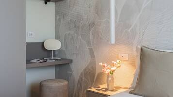 Une chambre moderne avec un lit, une table de chevet avec une lampe, un petit tabouret et un mur au motif texturé.