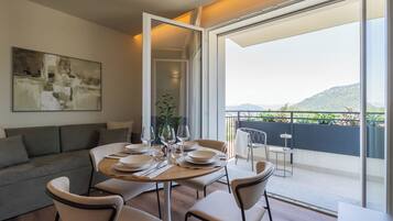 Un'area pranzo moderna con un tavolo rotondo apparecchiato per quattro persone, un divano grigio e un'ampia finestra che si affaccia su un paesaggio montuoso.