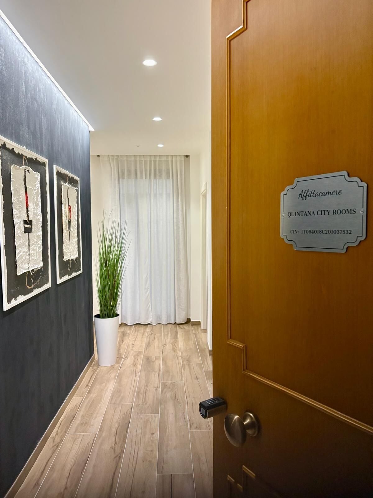 En hotellentréd med en trädörr, en skylt som visar ”Quintana City Rooms”, och en krukväxt.