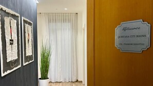 A hotel entrance with a wooden door, a sign indicating 'Quintana City Rooms,' and a potted plant.