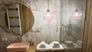 A modern bathroom with a marble wall, a wooden vanity, a pink basin, and two pink pendant lights.