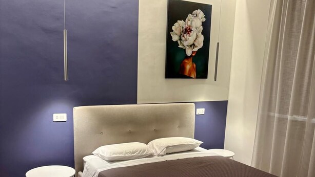 A modern bedroom with a large bed, a round side table, and a painting of flowers on the wall.