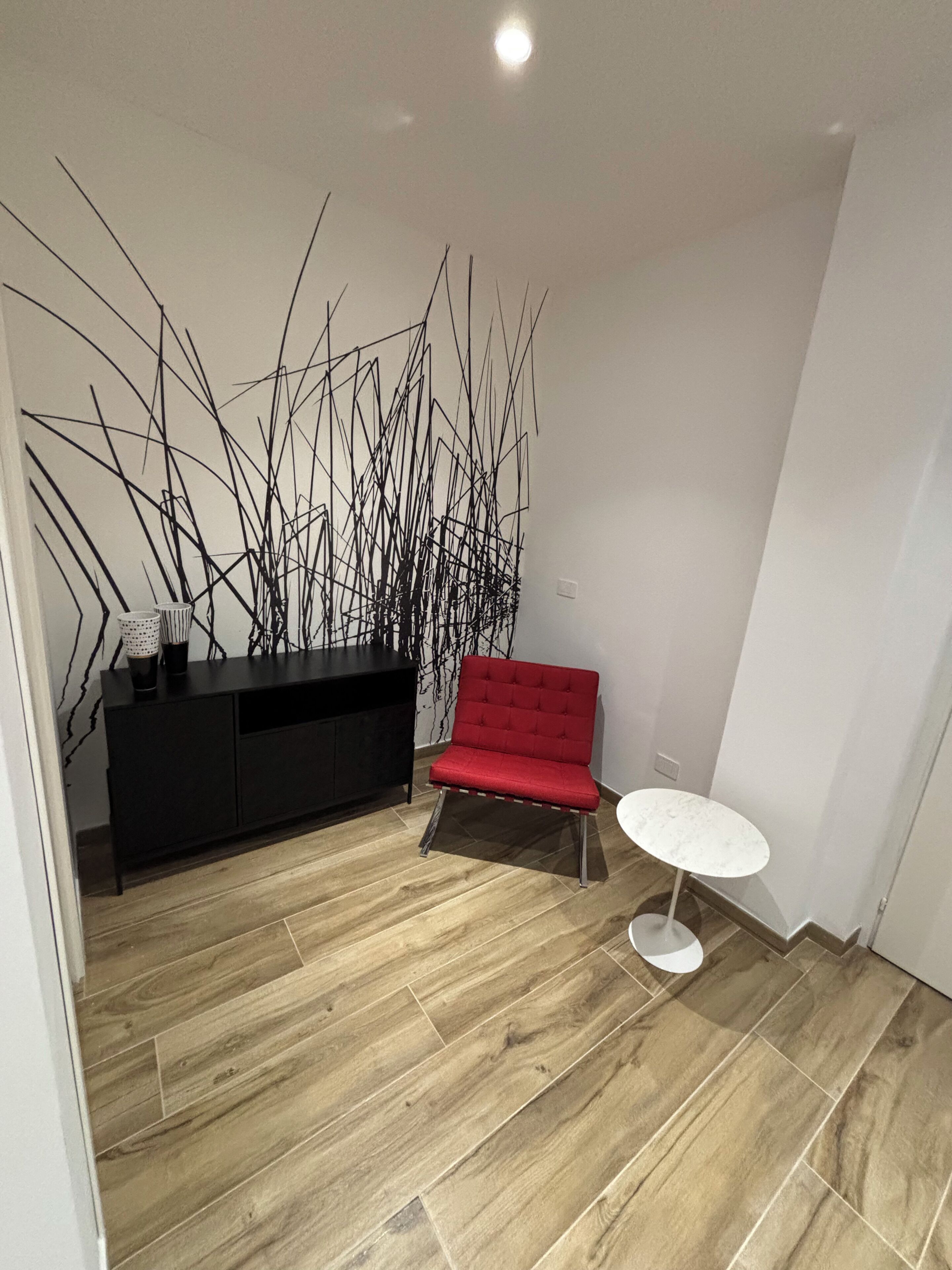 A modern room with a wooden floor, a red chair, a white table, and a black cabinet.
