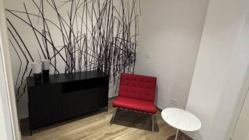 A modern room with a wooden floor, a red chair, a white table, and a black cabinet.