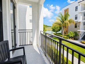 A balcony with a view of a lake, palm trees, and a building with multiple floors. - Luxury North Retreat with Pool and Gym (Naples)